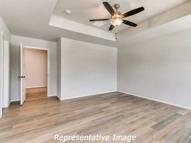 unfurnished room with baseboards, a raised ceiling, wood finished floors, and a ceiling fan