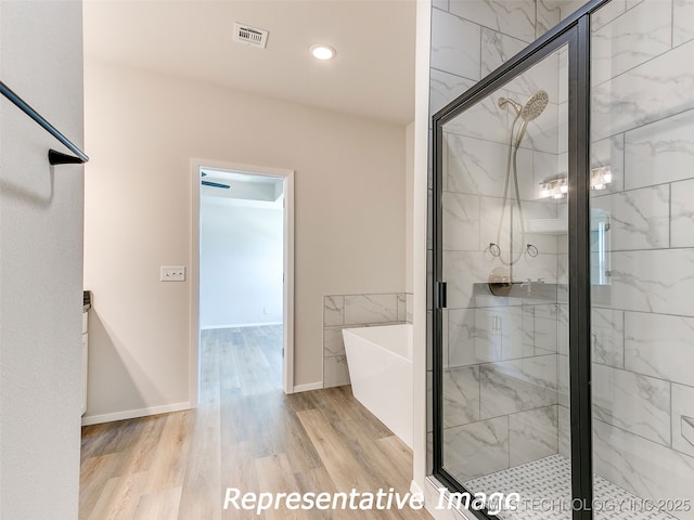 full bathroom featuring visible vents, a shower stall, baseboards, a freestanding bath, and wood finished floors