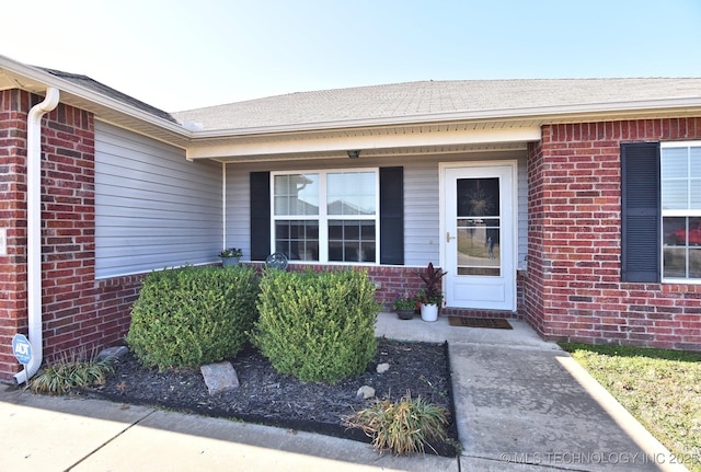 doorway to property with brick siding and roof with shingles