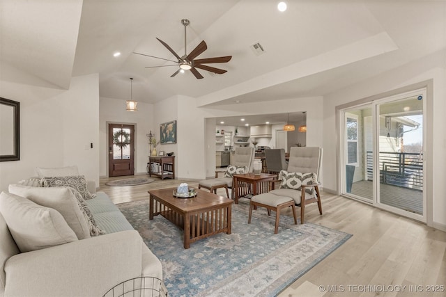 living room featuring vaulted ceiling, plenty of natural light, visible vents, and light wood-type flooring