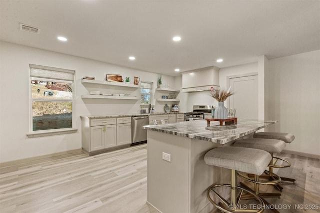 kitchen with light stone counters, light wood finished floors, a breakfast bar, open shelves, and appliances with stainless steel finishes