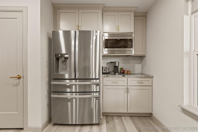 kitchen with baseboards, appliances with stainless steel finishes, light stone countertops, and light wood finished floors