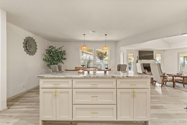 kitchen featuring light wood-type flooring, visible vents, light stone countertops, and decorative light fixtures