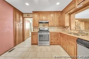 kitchen with backsplash, under cabinet range hood, light countertops, appliances with stainless steel finishes, and a sink