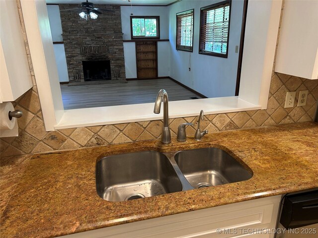 4331 S Norfolk Ave, Tulsa, OK 74105 - kitchen featuring a sink, decorative backsplash, a stone fireplace, white cabinets, and a ceiling fan