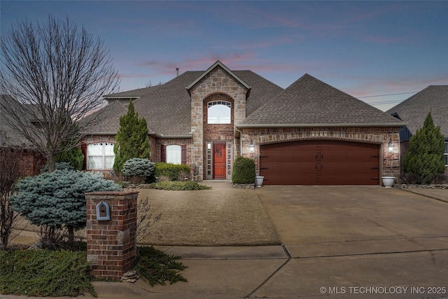 french country home featuring brick siding, roof with shingles, and driveway