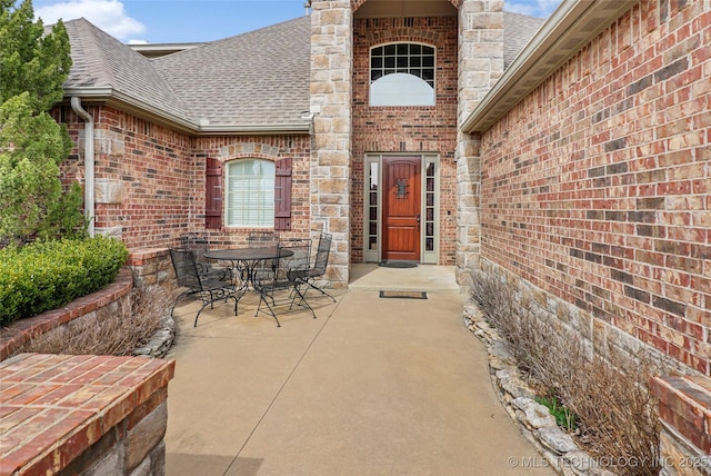 property entrance featuring brick siding, roof with shingles, a chimney, outdoor dining area, and a patio area