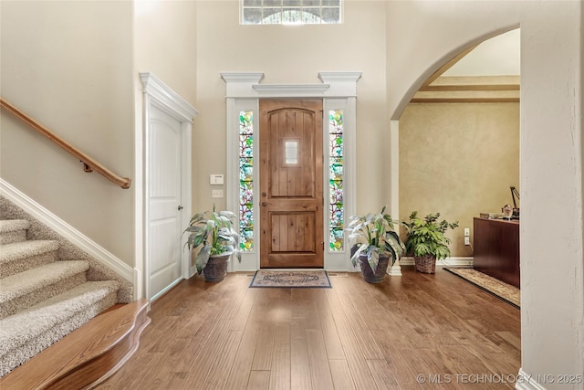 entrance foyer featuring stairs, wood finished floors, arched walkways, and a towering ceiling