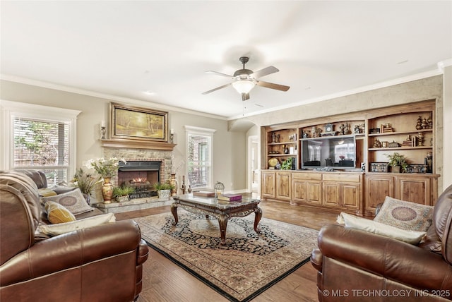 living room featuring a fireplace, light wood-type flooring, crown molding, and a ceiling fan