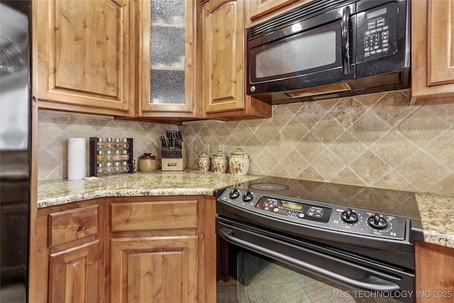 kitchen with glass insert cabinets, light stone countertops, tasteful backsplash, and black appliances