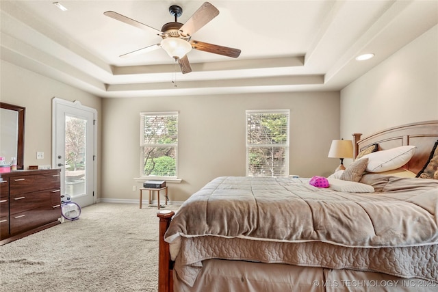 carpeted bedroom featuring multiple windows, a raised ceiling, and access to outside