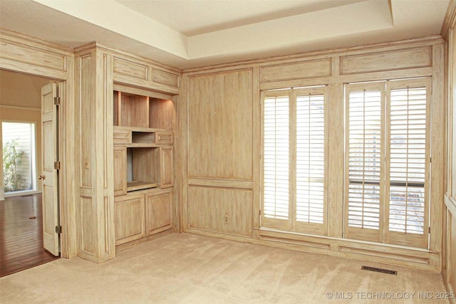 empty room with light colored carpet, visible vents, and wood walls