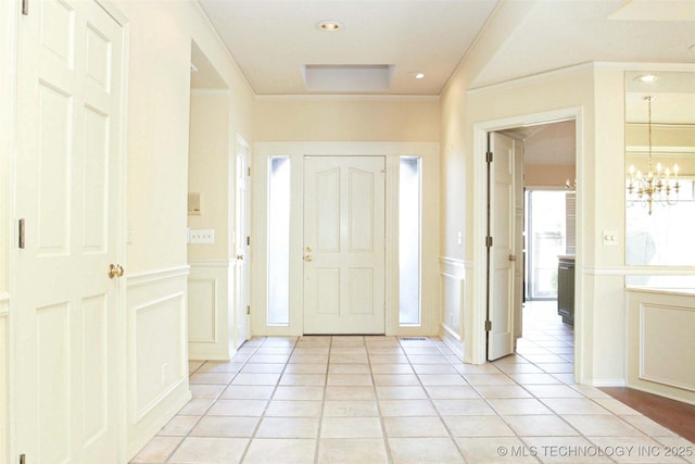 entryway with an inviting chandelier, a decorative wall, light tile patterned floors, and crown molding