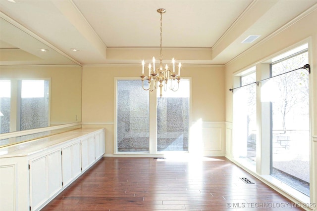 unfurnished dining area with a wainscoted wall, a raised ceiling, visible vents, and dark wood-style flooring