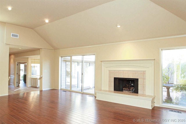 unfurnished living room with a tiled fireplace, visible vents, wood finished floors, and vaulted ceiling