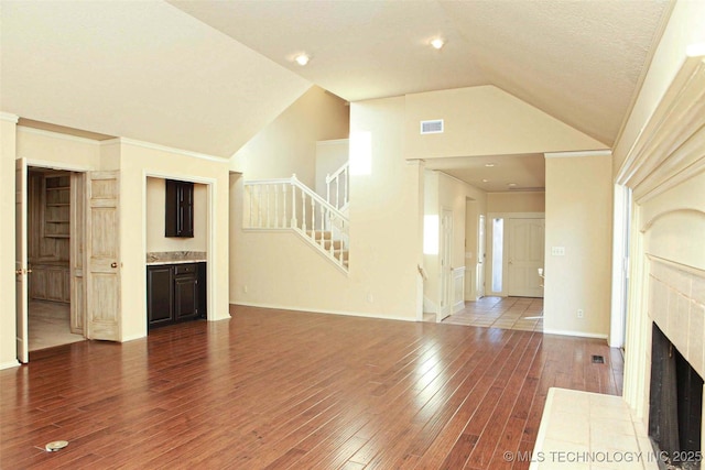 unfurnished living room featuring visible vents, stairway, wood-type flooring, a fireplace, and lofted ceiling