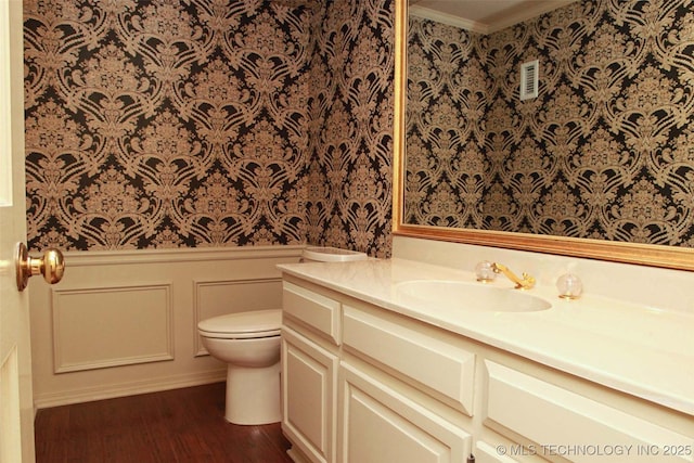 bathroom with vanity, a wainscoted wall, wallpapered walls, a decorative wall, and toilet