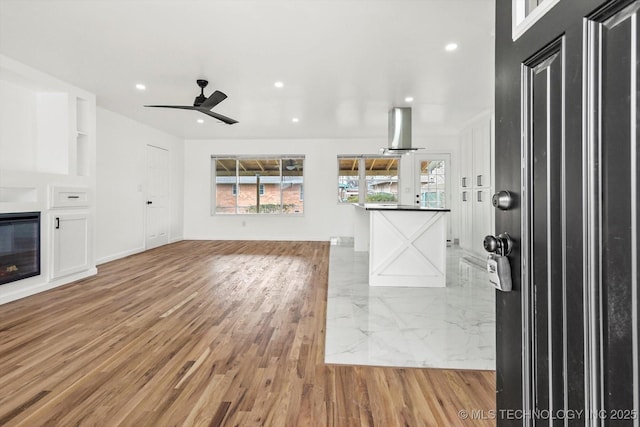 unfurnished living room featuring a glass covered fireplace, recessed lighting, light wood finished floors, and a ceiling fan