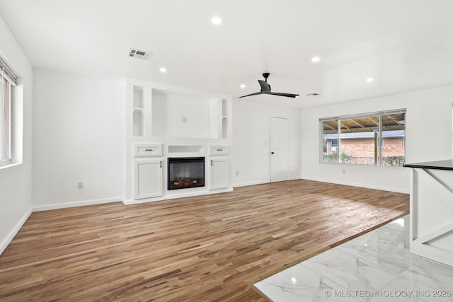 unfurnished living room featuring light wood finished floors, visible vents, built in shelves, baseboards, and a fireplace