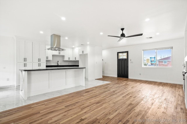 kitchen with visible vents, light wood-style flooring, island exhaust hood, dark countertops, and white cabinetry