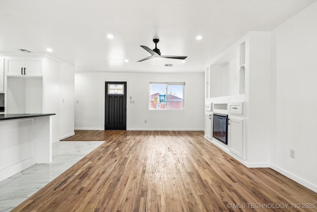 unfurnished living room featuring a glass covered fireplace, visible vents, a ceiling fan, and baseboards