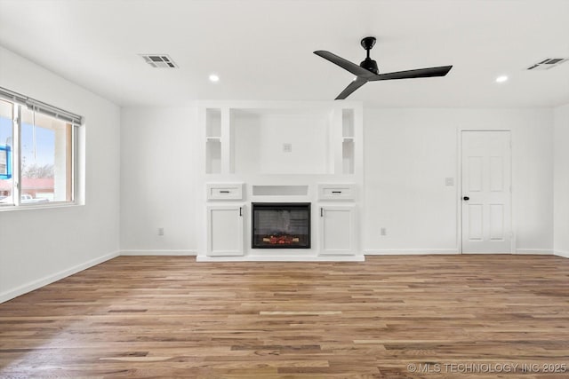 unfurnished living room featuring light wood finished floors, visible vents, a ceiling fan, and a glass covered fireplace