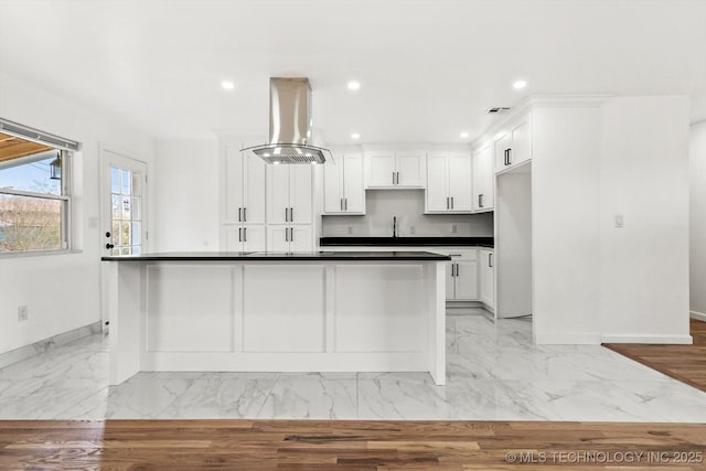 kitchen with dark countertops, white cabinets, island exhaust hood, and marble finish floor