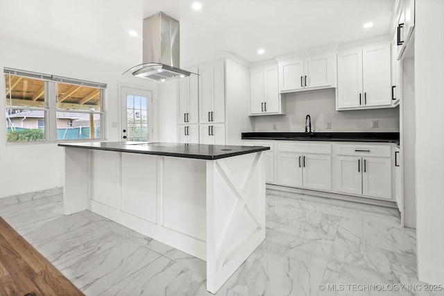 kitchen with a sink, white cabinets, dark countertops, marble finish floor, and island range hood