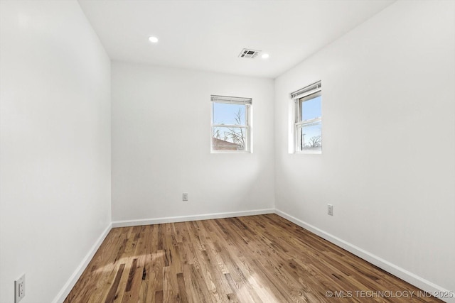 empty room featuring wood finished floors, recessed lighting, baseboards, and visible vents