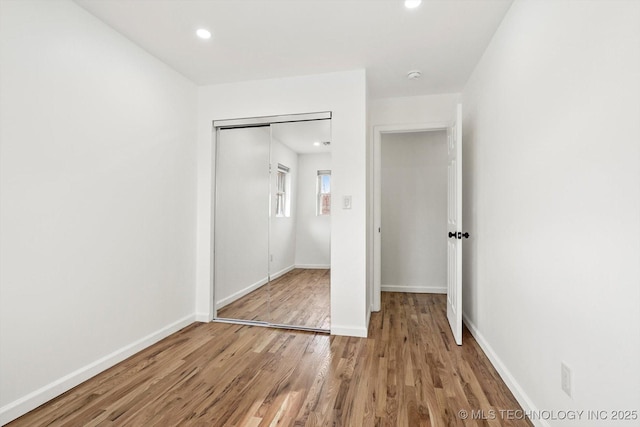 unfurnished bedroom with recessed lighting, a closet, baseboards, and wood finished floors