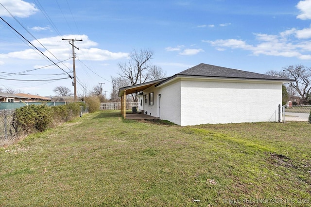 view of side of home with a patio, a yard, a fenced backyard, a shingled roof, and brick siding