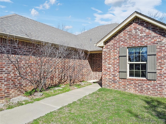 exterior space with brick siding, a lawn, and roof with shingles