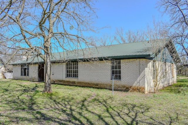 view of home's exterior featuring a yard, brick siding, and metal roof