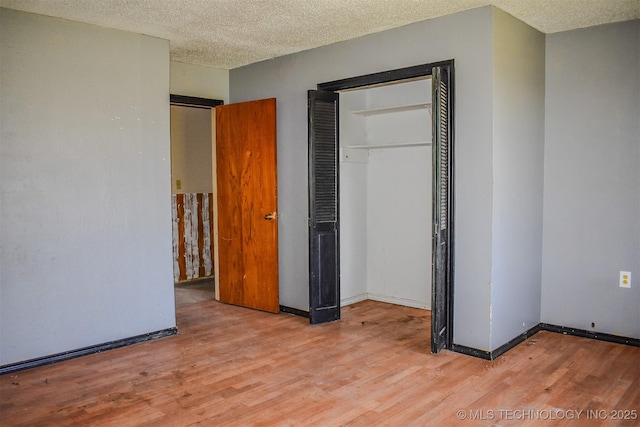 unfurnished bedroom with baseboards, light wood-style floors, a closet, and a textured ceiling