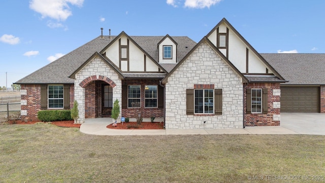 english style home featuring brick siding, a front lawn, concrete driveway, roof with shingles, and stucco siding