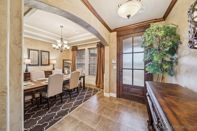 entryway featuring baseboards, a tray ceiling, arched walkways, crown molding, and a notable chandelier