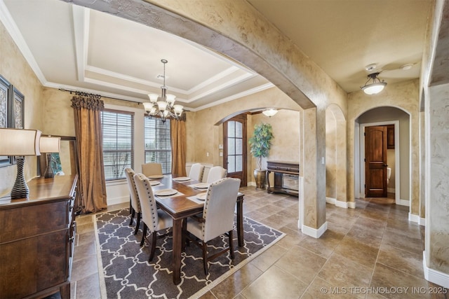 dining room featuring baseboards, an inviting chandelier, a tray ceiling, arched walkways, and crown molding