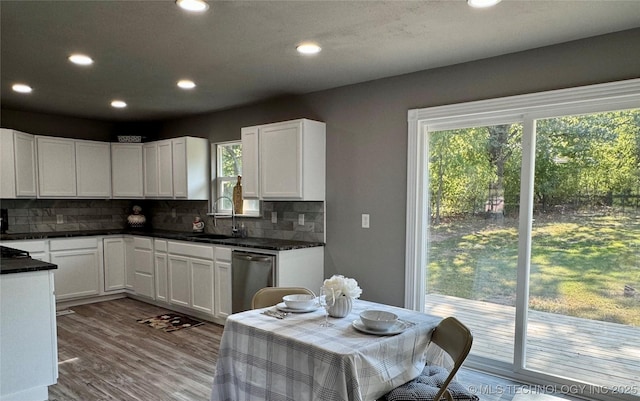 kitchen with a sink, plenty of natural light, stainless steel dishwasher, dark countertops, and white cabinets