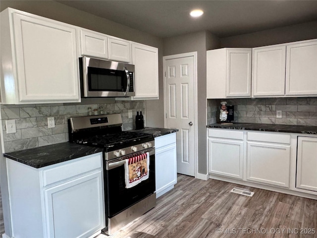 kitchen with tasteful backsplash, white cabinets, appliances with stainless steel finishes, and light wood-type flooring