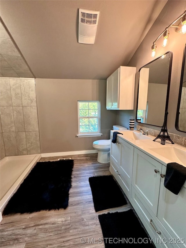 bathroom featuring wood finished floors, lofted ceiling, double vanity, a sink, and toilet