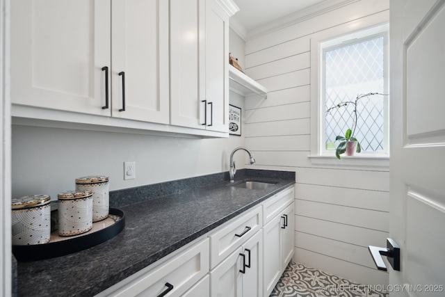 kitchen with a sink, dark stone counters, wooden walls, and white cabinets