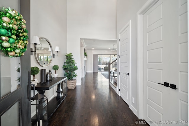 foyer entrance with a ceiling fan, dark wood-style flooring, a high ceiling, baseboards, and stairs