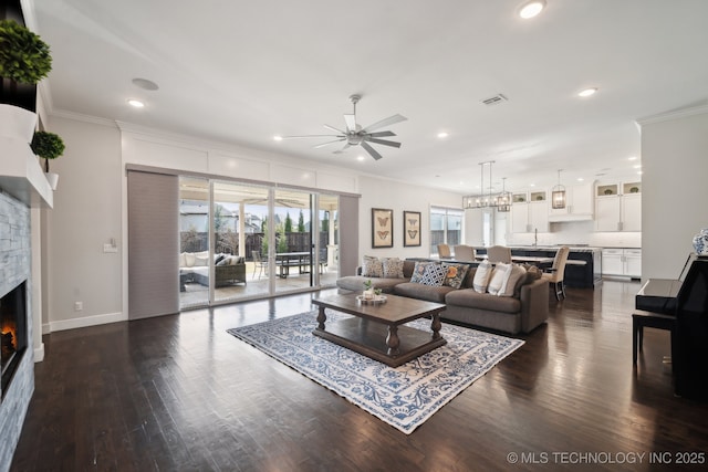 living area featuring a stone fireplace, recessed lighting, dark wood-style flooring, and ornamental molding