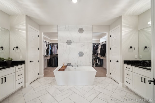 bathroom featuring a freestanding tub, marble finish floor, vanity, tile walls, and a spacious closet