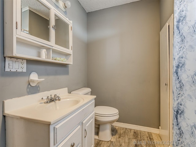 bathroom featuring baseboards, toilet, vanity, wood finished floors, and a textured ceiling