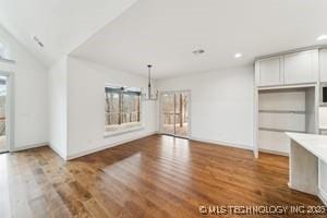 unfurnished living room featuring vaulted ceiling, a healthy amount of sunlight, and wood finished floors