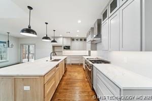 kitchen with a spacious island, a sink, glass insert cabinets, wall chimney range hood, and stainless steel gas stove