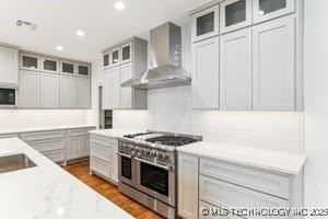 kitchen featuring glass insert cabinets, wall chimney range hood, range with two ovens, recessed lighting, and dark wood-style flooring