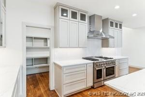 kitchen featuring dark wood-type flooring, double oven range, recessed lighting, wall chimney range hood, and glass insert cabinets