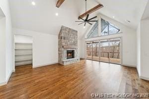 unfurnished living room with beamed ceiling, high vaulted ceiling, wood finished floors, a large fireplace, and ceiling fan